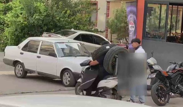 Otomobil lastiğini boynuna asan kuryenin ilginç taşıma yöntemi kameraya yansıdı